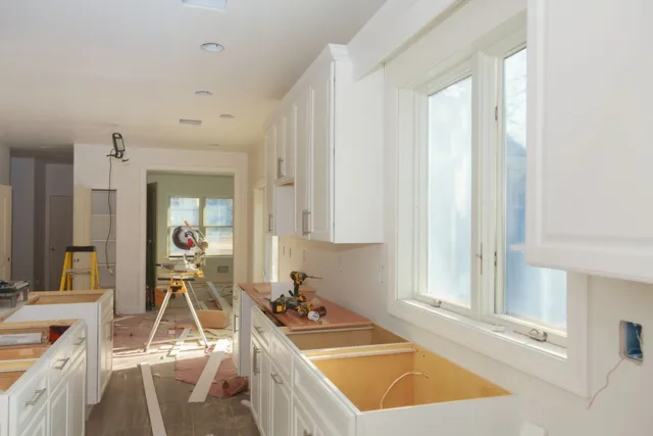 A kitchen with white cabinets and wood floors.