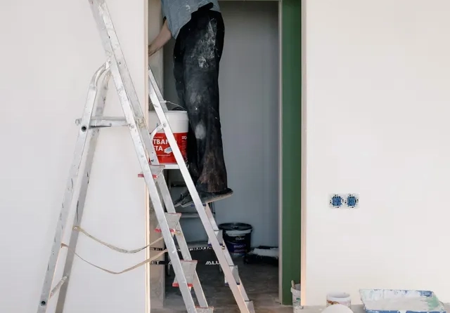 A man standing on top of a ladder painting.