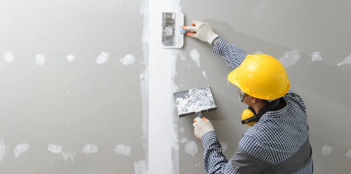 A man in yellow hard hat working on wall.